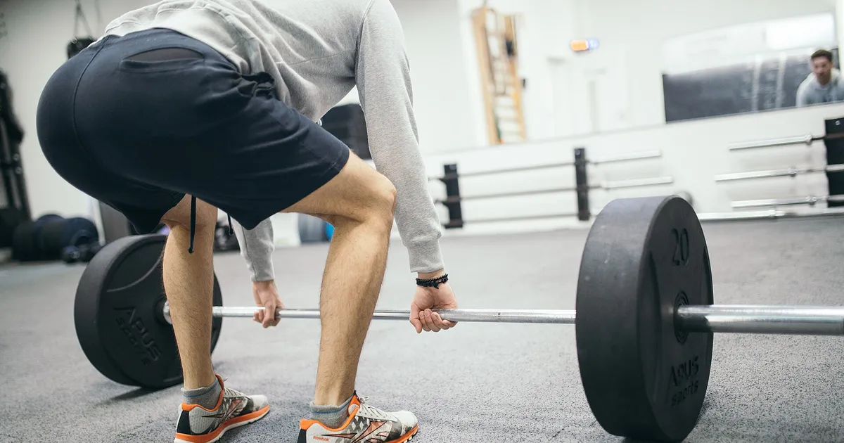 A man set up over a loaded barbell in the start position of a deadlift, gripping the bar with bumper plates loaded